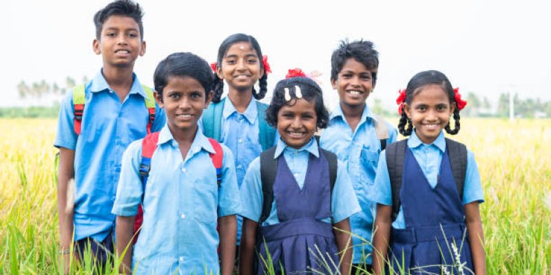group of happy smiling village school kids in uniform standing at middle paddy field by looking camera - concept of friendship, education and togetherness.